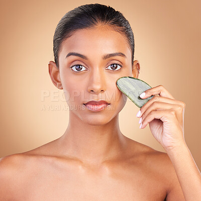 Buy stock photo Skincare, beauty and portrait of Indian woman with gua sha, facial treatment and wellness with spa stone. Salon, dermatology and girl on brown background with cosmetics, face massage and luxury tools