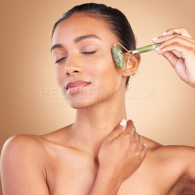 Buy stock photo Face, massage and beauty with a model woman in studio on a brown background for natural antiaging skincare. Wellness, luxury and product with an attractive young female using a roller for skin lift