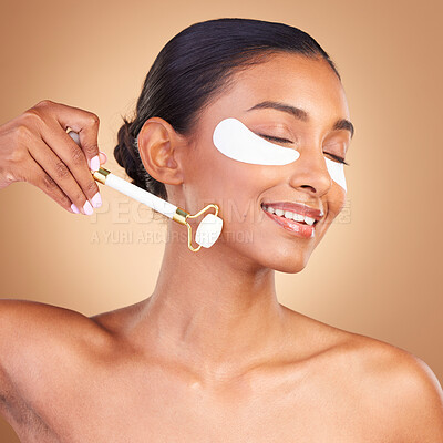 Buy stock photo Roller, eye patch and beauty with Indian woman in studio for facial, spa treatment and glow. Self care, cosmetics and hydration with female model on brown background for mask, product and youth