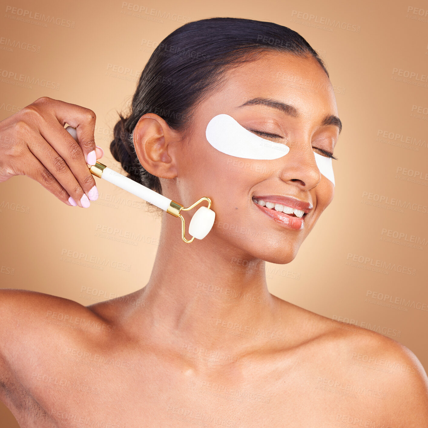 Buy stock photo Roller, eye patch and beauty with Indian woman in studio for facial, spa treatment and glow. Self care, cosmetics and hydration with female model on brown background for mask, product and youth