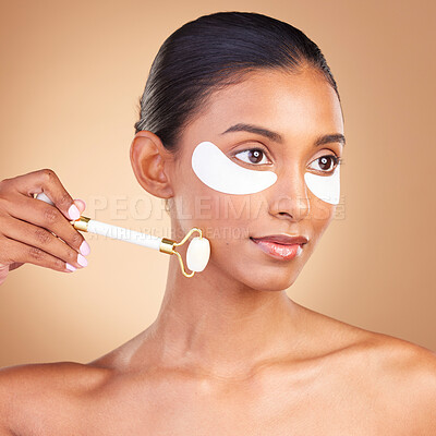 Buy stock photo Skincare, eye patch and roller with Indian woman in studio for facial, spa treatment and glow. Self care, cosmetics and hydration with female model on brown background for mask, product and youth