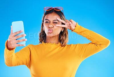 Buy stock photo Selfie, studio and peace sign of a woman influencer taking a profile picture for social media. Isolated, blue background and silly hands gesture of a gen z female with a kiss feeling happy and fun