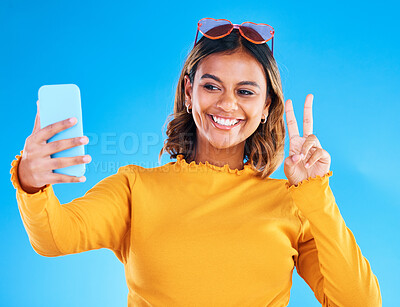 Buy stock photo Selfie smile, studio and peace sign of a woman influencer taking a profile picture for social media. Isolated, blue background and emoji hands gesture of a gen z female with feeling happy and fun