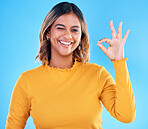 Ok, portrait and happy woman wink on blue background, studio and agreement of support. Female model, smile and okay hands of success, yes and winner of perfect emoji, thank you and review approval 