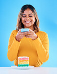 Woman, cake and studio with a phone for social media picture with a smile and excited to eat. Happy female person on blue background with rainbow color dessert for birthday or influencer celebration
