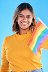 Portrait, flag and gay with a woman on a blue background in studio feeling proud of her lgbt status. Smile, freedom and equality with a happy young female holding a rainbow symbol of inclusion
