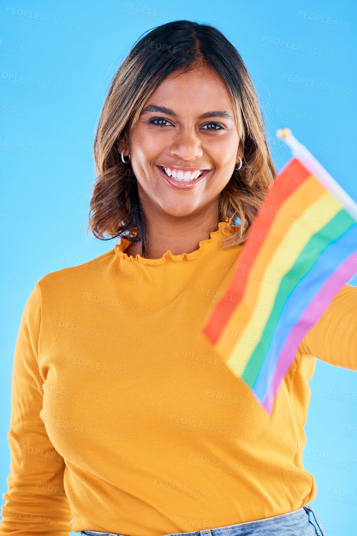 Buy stock photo Portrait, flag and gay with a woman on a blue background in studio feeling proud of her lgbt status. Smile, freedom and equality with a happy young female holding a rainbow symbol of inclusion