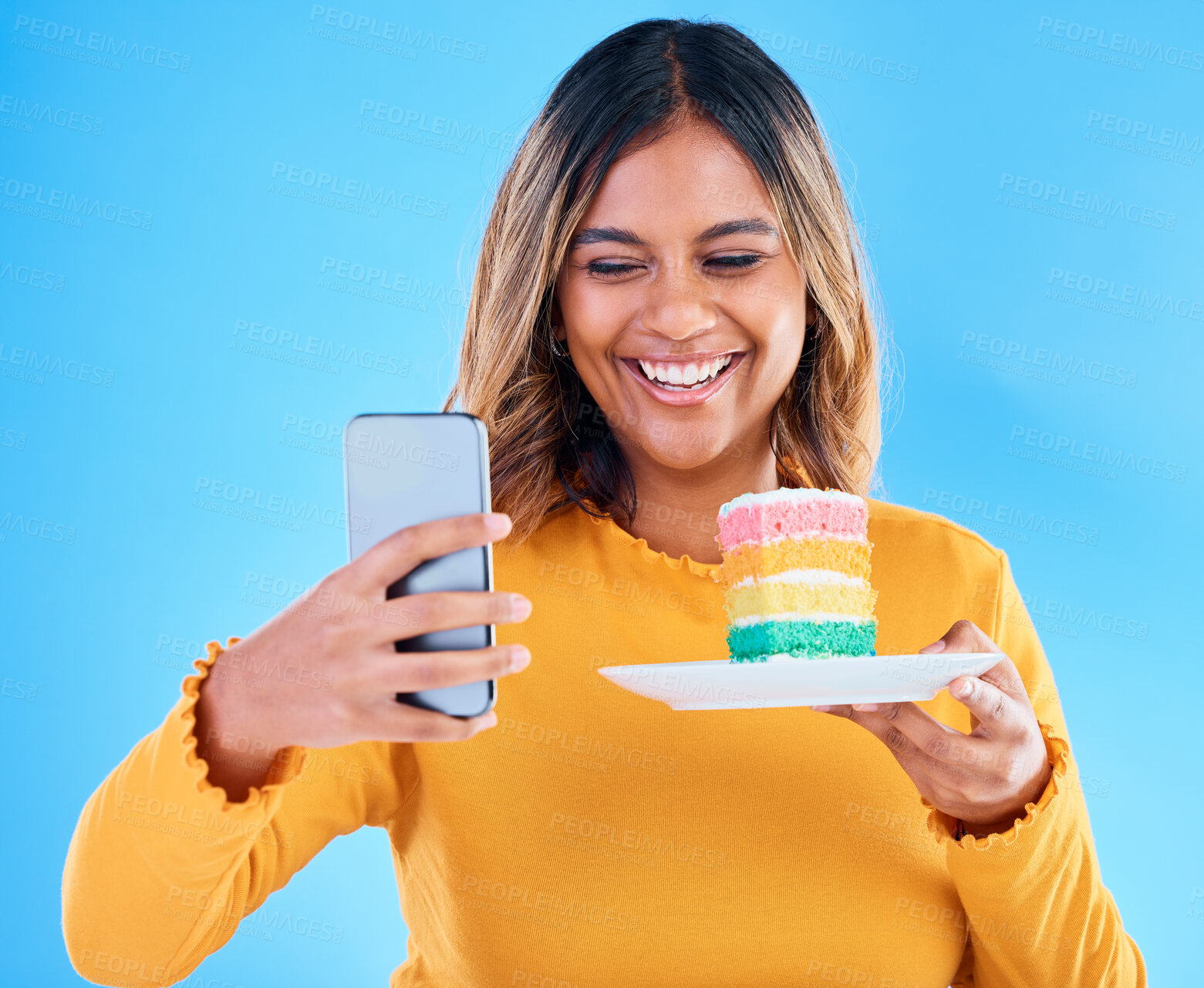 Buy stock photo Woman, cake and smile selfie in studio for social media profile picture and excited to eat. Happy female laughing on blue background with rainbow color dessert for birthday or influencer celebration