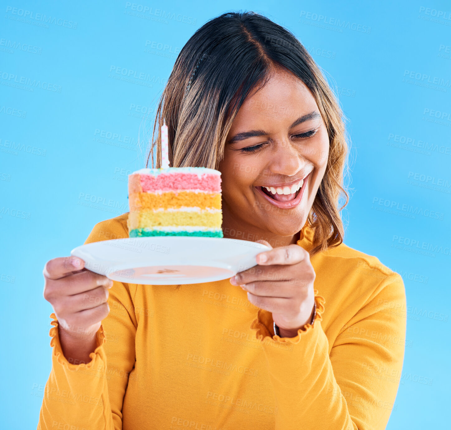 Buy stock photo Woman, birthday cake and candle studio with a smile and excited to eat. Happy female person laughing on blue background with sweet rainbow color dessert for celebration and happiness on face