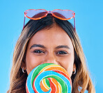 Portrait, giant lollipop and a woman on a blue background in studio wearing heart glasses for fashion. Face, candy and sweet with an attractive young female eating a snack while feeling happy