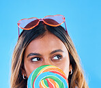 Thinking, lollipop and a woman on a blue background in studio wearing heart glasses for fashion. Idea, candy and sweet with an attractive young female eating a giant snack while feeling thoughtful