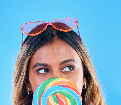 Buy stock photo Thinking, lollipop and a woman on a blue background in studio wearing heart glasses for fashion. Idea, candy and sweet with an attractive young female eating a giant snack while feeling thoughtful