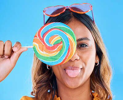 Buy stock photo Portrait, lollipop and tongue with a woman on a blue background in studio wearing heart glasses for fashion. Funny face, candy and sweet with a young female eating a giant snack while feeling silly