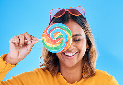 Buy stock photo Laughing, lollipop and a woman on a blue background in studio wearing heart glasses for fashion. Funny, candy and sweet with an attractive young female eating a giant snack while feeling silly