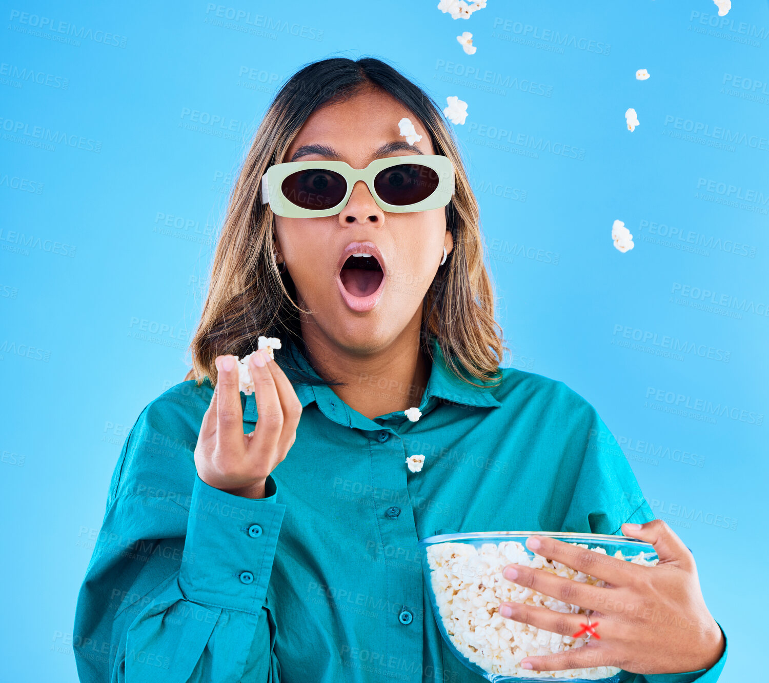 Buy stock photo 3D movie, popcorn and surprise with a woman in studio on a blue background looking shocked while eating a snack. Portrait, glasses and wow with an attractive young female watching video entertainment