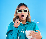 3D movie, popcorn and wow with a woman in studio on a blue background looking shocked while eating a snack. Portrait, glasses and video entertainment with an attractive young female feeling surprised