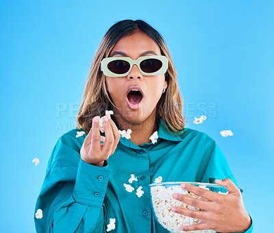Buy stock photo 3D movie, popcorn and wow with a woman in studio on a blue background looking shocked while eating a snack. Portrait, glasses and video entertainment with an attractive young female feeling surprised