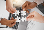 Hands, puzzle piece and overhead with a business team in the office, working in collaboration on a project. Teamwork, jigsaw and laptop with a diverse group of people at work together from above