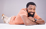 Portrait, happy and a black man lying on the floor isolated on a grey studio background. Smile, relax and a calm African guy relaxing, smiling and looking confident on the ground of a backdrop