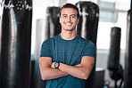 Portrait, punching bag with a man boxer in the gym, standing arms crossed for fitness or motivation. Happy, exercise and confidence with a handsome young male training for boxing or a fight