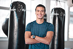 Portrait, boxing and punching bag with a man in the gym, standing arms crossed for fitness or motivation. Happy, exercise and confidence with a handsome young male boxer training for a fight