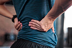 Hands, back and injury with a sports man holding a muscle in pain while training in a gym for health. Fitness, accident and anatomy with a male athlete suffering from an injured body during exercise