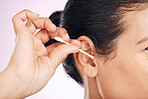 Woman, cotton and cleaning ear in studio in cropped closeup for wellness by pink background. Model hand, self care and clean with hygiene, earwax and natural product for healthy hearing by background