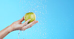 Water, apple cleaning and hands with fruit for wellness, healthcare and beauty self care. Healthy food, green and natural skincare with a hand holding health snack for diet in blue background studio