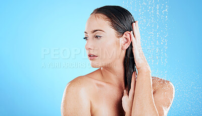 Buy stock photo Shower, water and face of woman on blue background for grooming, cleaning and body wellness in studio. Skincare, bathroom mockup and serious girl model washing hair for hygiene, hydration and beauty