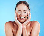 Shower, water and woman in a studio feeling happy from cleaning and skincare. Wellness, splash and beauty routine of a female model excited from dermatology and self care with blue background