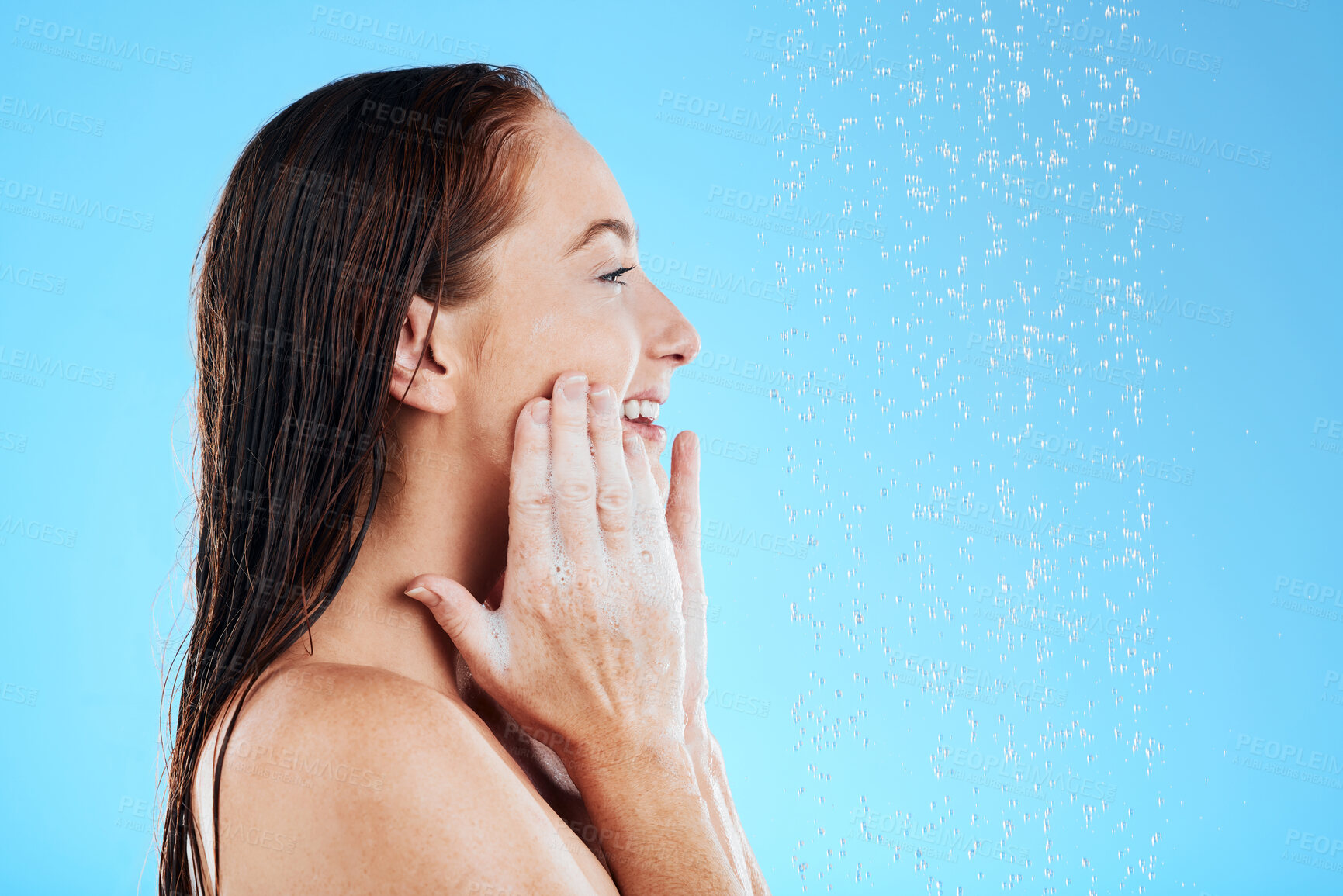 Buy stock photo Shower, water and happy woman with soap on face in studio, blue background and skincare cleaning. Female model washing facial with foam, wet drops and beauty of self care, glow and smile on backdrop