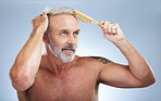 Mature man, brush hair and scalp treatment in a studio with a male model doing beauty routine. Wellness lifestyle, hairstyle care and barber and hairdresser comb with an isolated grey background 
