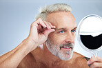 Senior man, tweezers and mirror check in a studio doing hair cleaning and grooming. Wellness, dermatology and beauty routine of a mature male model care with grey background and steel tools for face