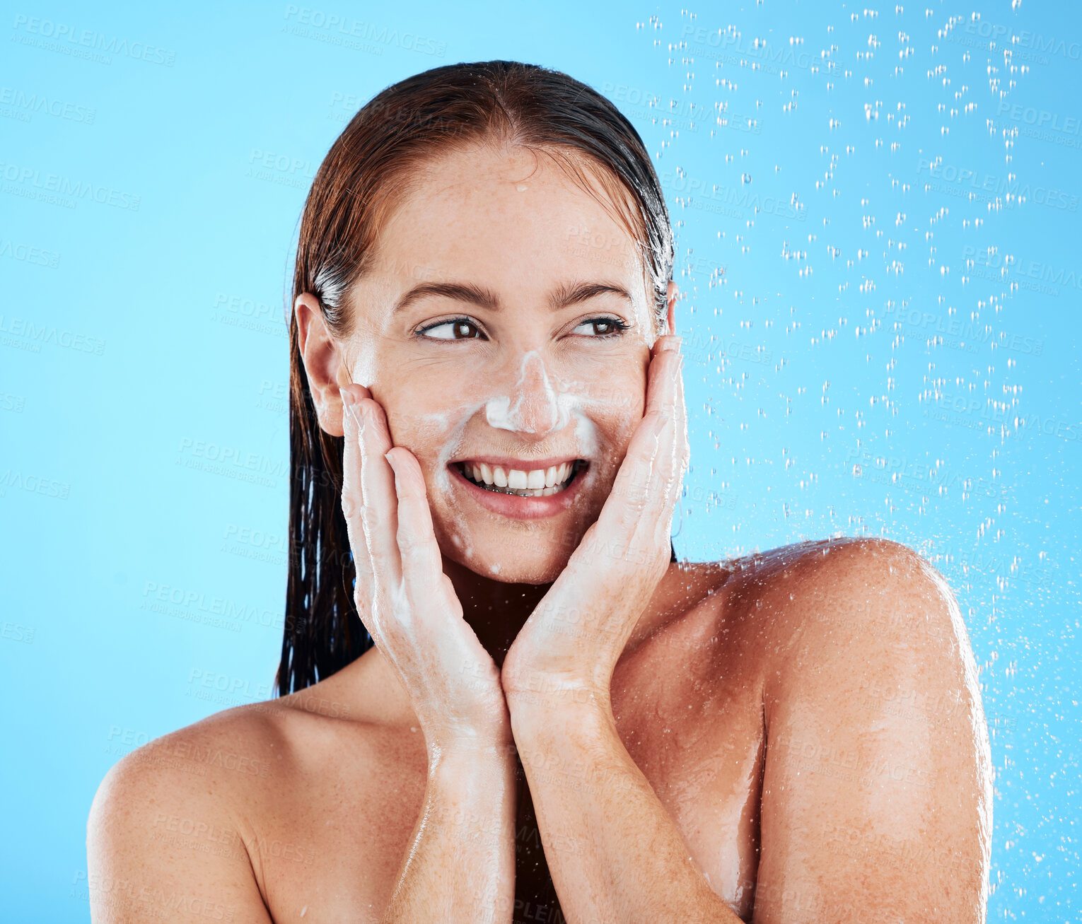 Buy stock photo Woman in shower, smile with hygiene and water drops, soap and clean with excited face on blue background. Facial, hands and skincare with happy female washing, foam  product and body care in studio