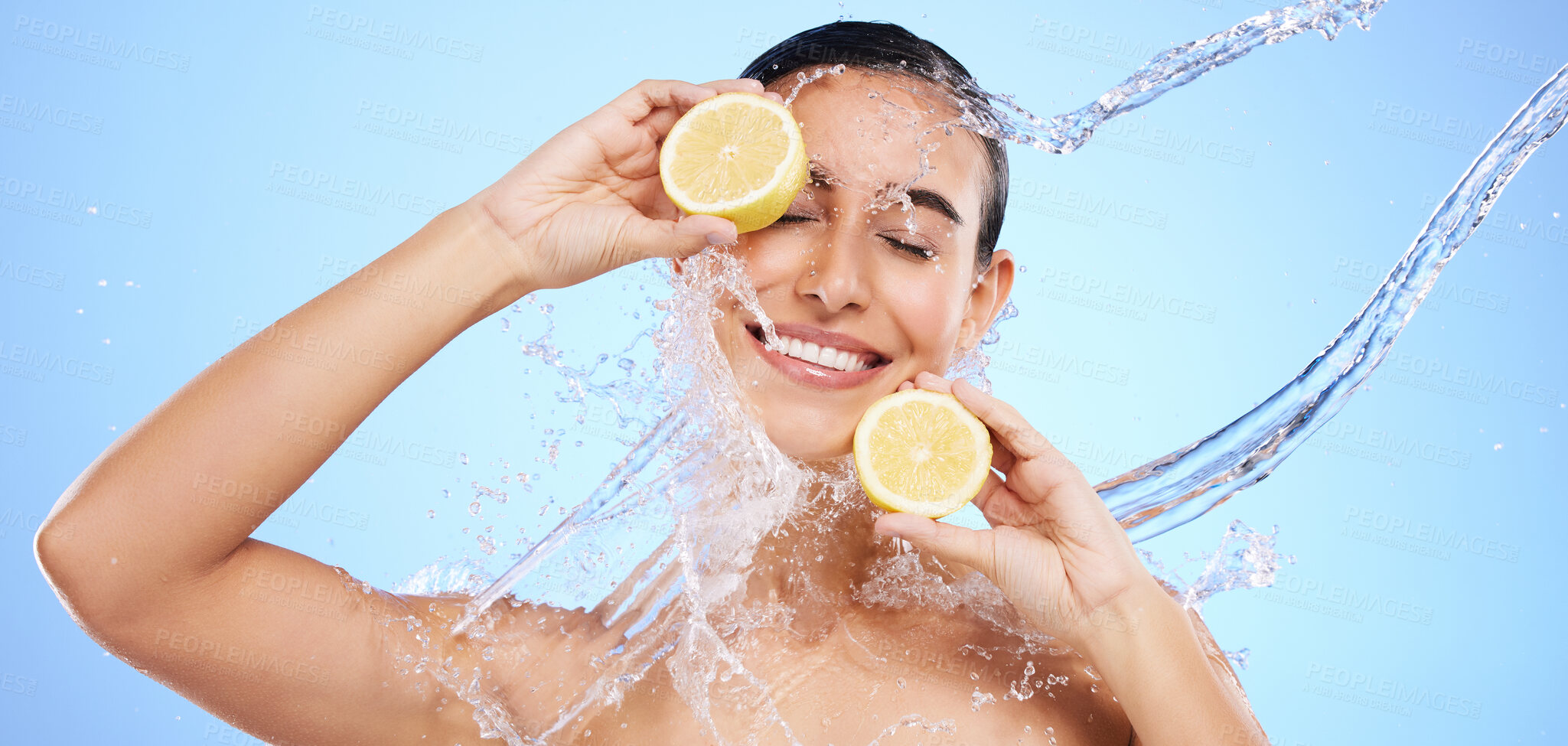 Buy stock photo Beauty, lemon and water splash with woman in studio for natural cosmetics, nutrition and detox. Glow, fruits and hydration with female on blue background for diet, clean face and vitamin c skincare