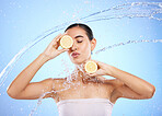 Beauty, kiss and water splash with woman and lemon in studio for natural cosmetics, nutrition and detox. Glow, fruits and hydration with female on blue background for vitamin c, face and skincare