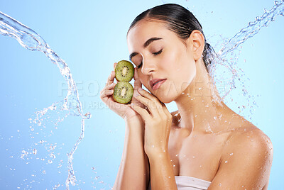 Buy stock photo Woman, water splash and face with kiwi in relax for skincare, hygiene or nutrition against blue studio background. Calm or relaxed female holding fruit in natural beauty cosmetics or facial treatment