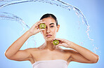 Kiwi, portrait and water splash of woman, beauty and wellness on studio blue background. Female model, shower and healthy fruits for natural benefits, detox skincare and dermatology of diet nutrition