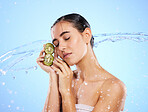 Kiwi, beauty and water splash of woman, skincare and wellness on studio blue background. Calm model, shower and healthy fruits for natural benefits, detox nutrition and dermatology with diet vitamins