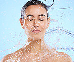 Water, splash and skincare with a woman in studio on a blue background for beauty, hygiene or hydration. Relax, wellness and cleaning with an attractive young female in the shower for self care