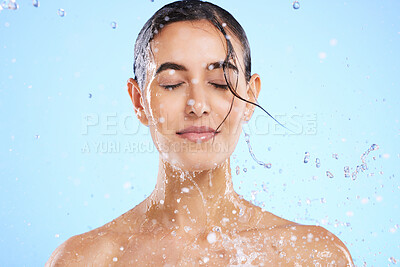 Buy stock photo Water splash, beauty and skincare with a woman in studio on a blue background for hygiene or hydration. Relax, wellness and cleaning with an attractive young female in the shower for self care