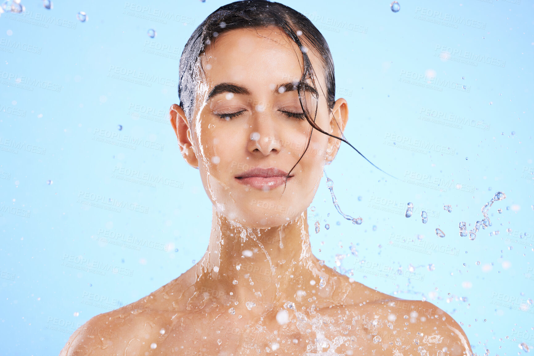 Buy stock photo Water splash, beauty and skincare with a woman in studio on a blue background for hygiene or hydration. Relax, wellness and cleaning with an attractive young female in the shower for self care