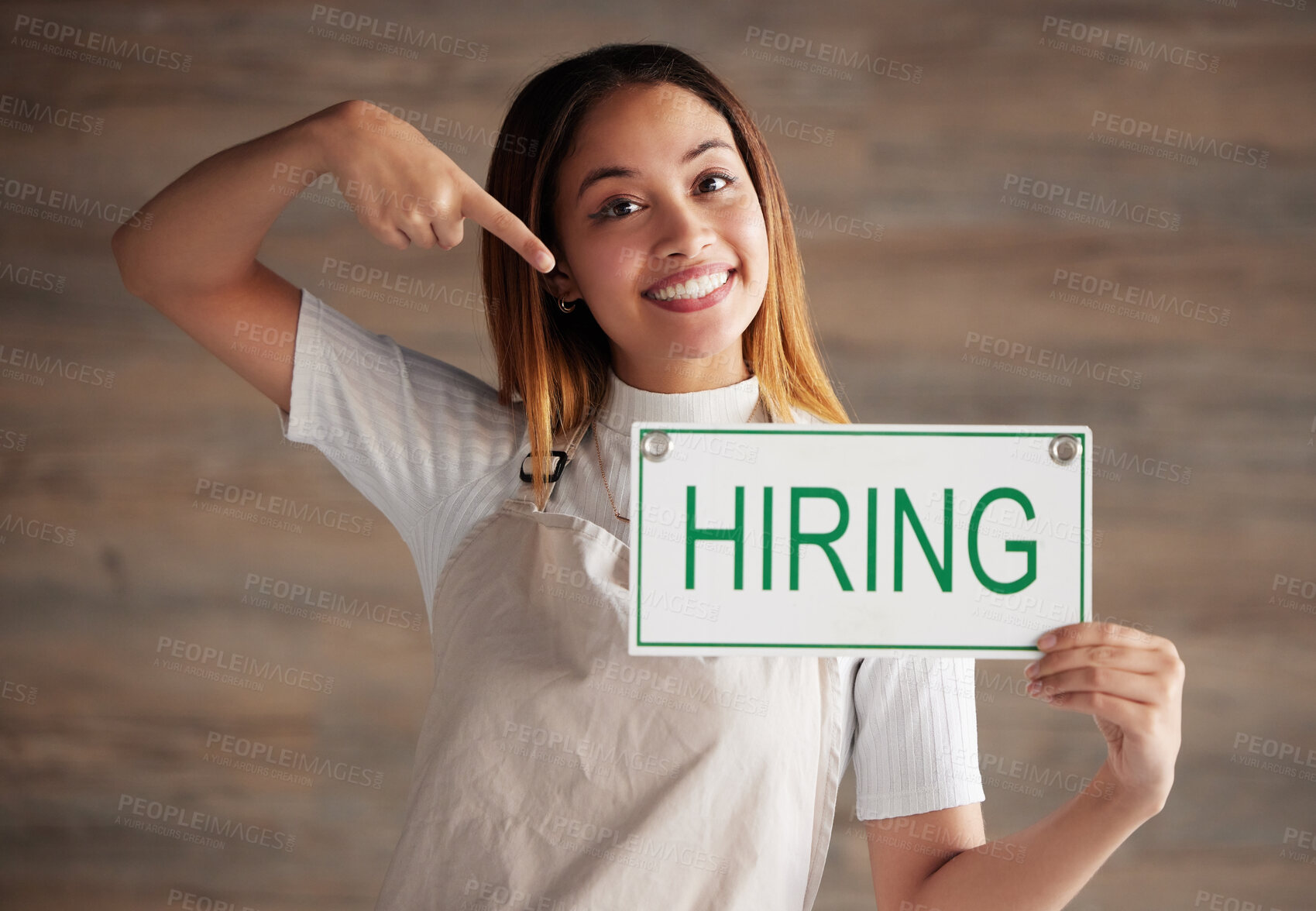 Buy stock photo Happy woman, portrait and pointing to hiring sign for small business recruitment, career or job opportunity against studio background. Female entrepreneur with apron holding billboard poster for hire