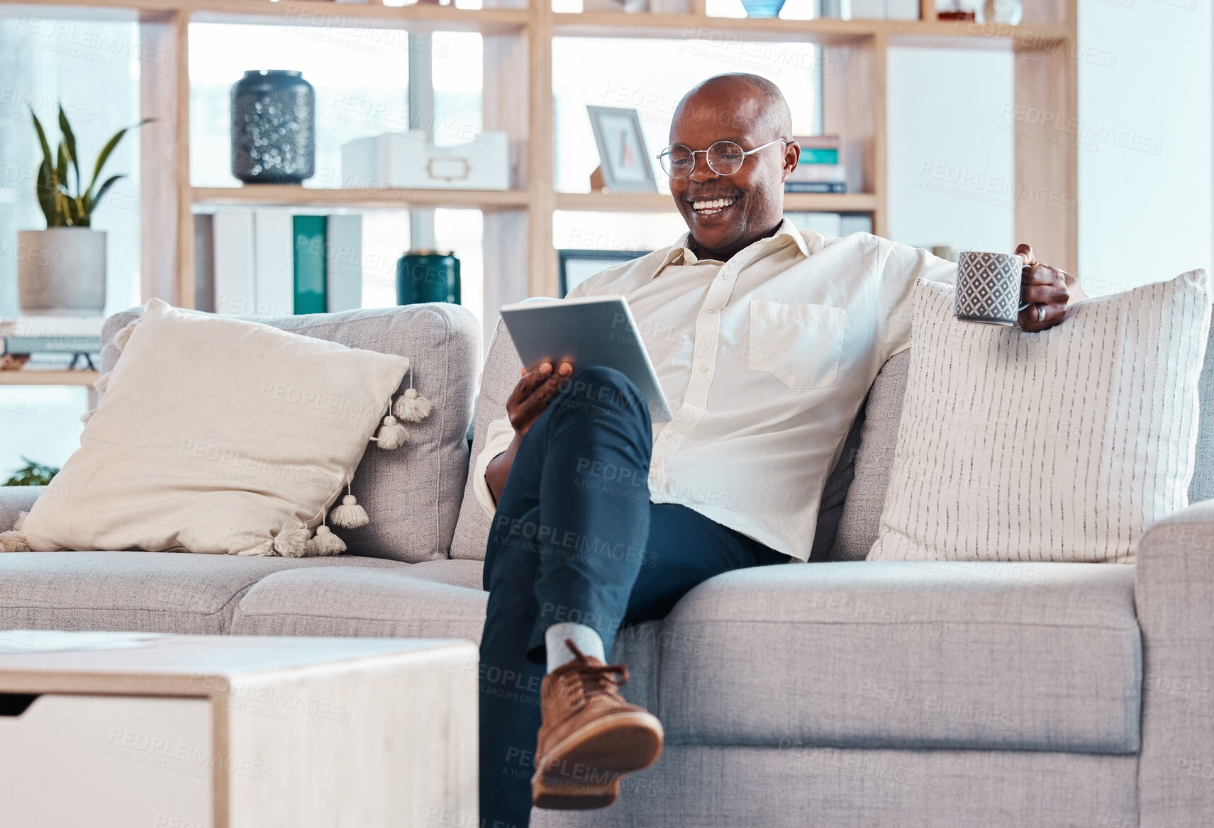 Buy stock photo Tablet, coffee break and relax with a black man on the sofa, sitting in the living room of his home or office. Business, tech or research with a male employee reading an online article while chilling