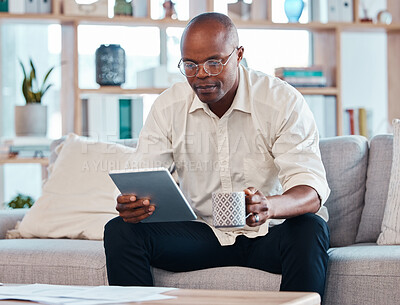 Buy stock photo Tablet, coffee and relax with a black man on the sofa, sitting in the living room of his home or office. Business, tech and research with a male employee reading an online article while on a break