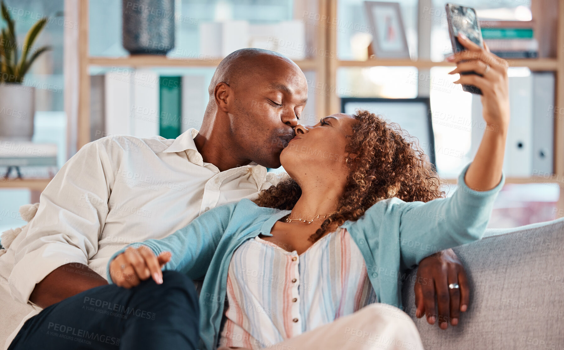 Buy stock photo Couple, selfie and kiss on sofa in home living room, bonding or having fun together. Interracial, romantic picture and black man and woman taking photo while kissing for love, memory or social media.