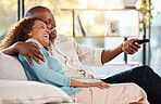 Couple, watching tv and laughing on sofa in home living room, bonding and hug. Interracial, television and funny black man and woman relax on couch streaming comedy movie, film or meme video online