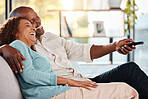 Couple, watching tv and laughing on sofa, hug in home living room and bonding. Interracial, television and funny black man and woman relax on couch streaming comedy movie, comic film or meme video.