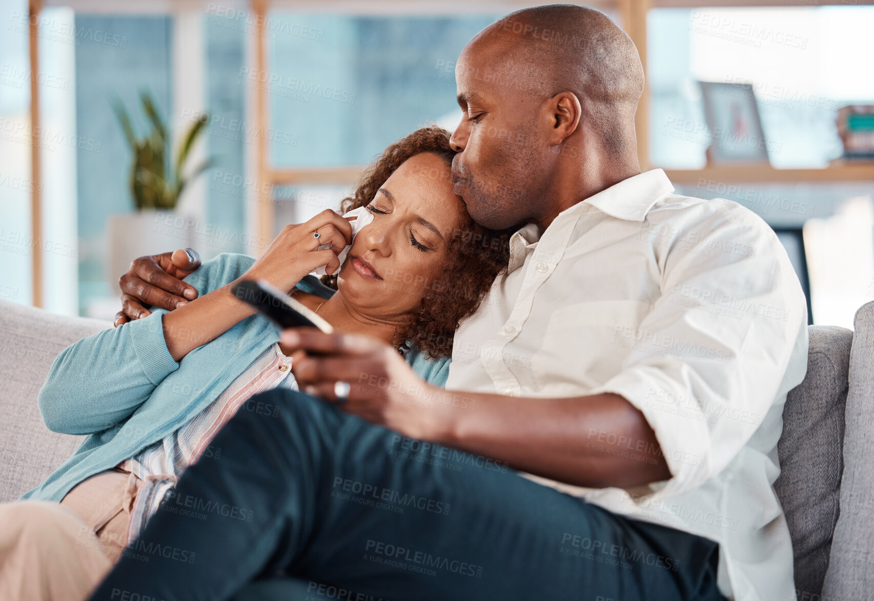 Buy stock photo Couple, watching tv and kiss while crying on sofa, hug in home living room and bonding. Interracial, television and black man and sad woman kissing on couch wipe tears streaming movie, film or video