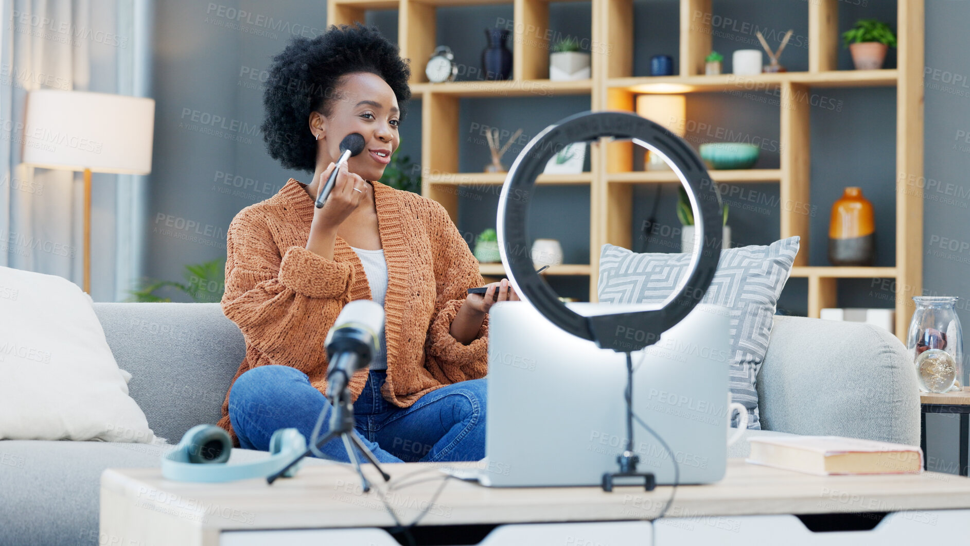 Buy stock photo Woman content creator recording a makeup tutorial for her beauty channel, blog or live streaming at home. Young African female influencer filming a video with cosmetic products in the living room.